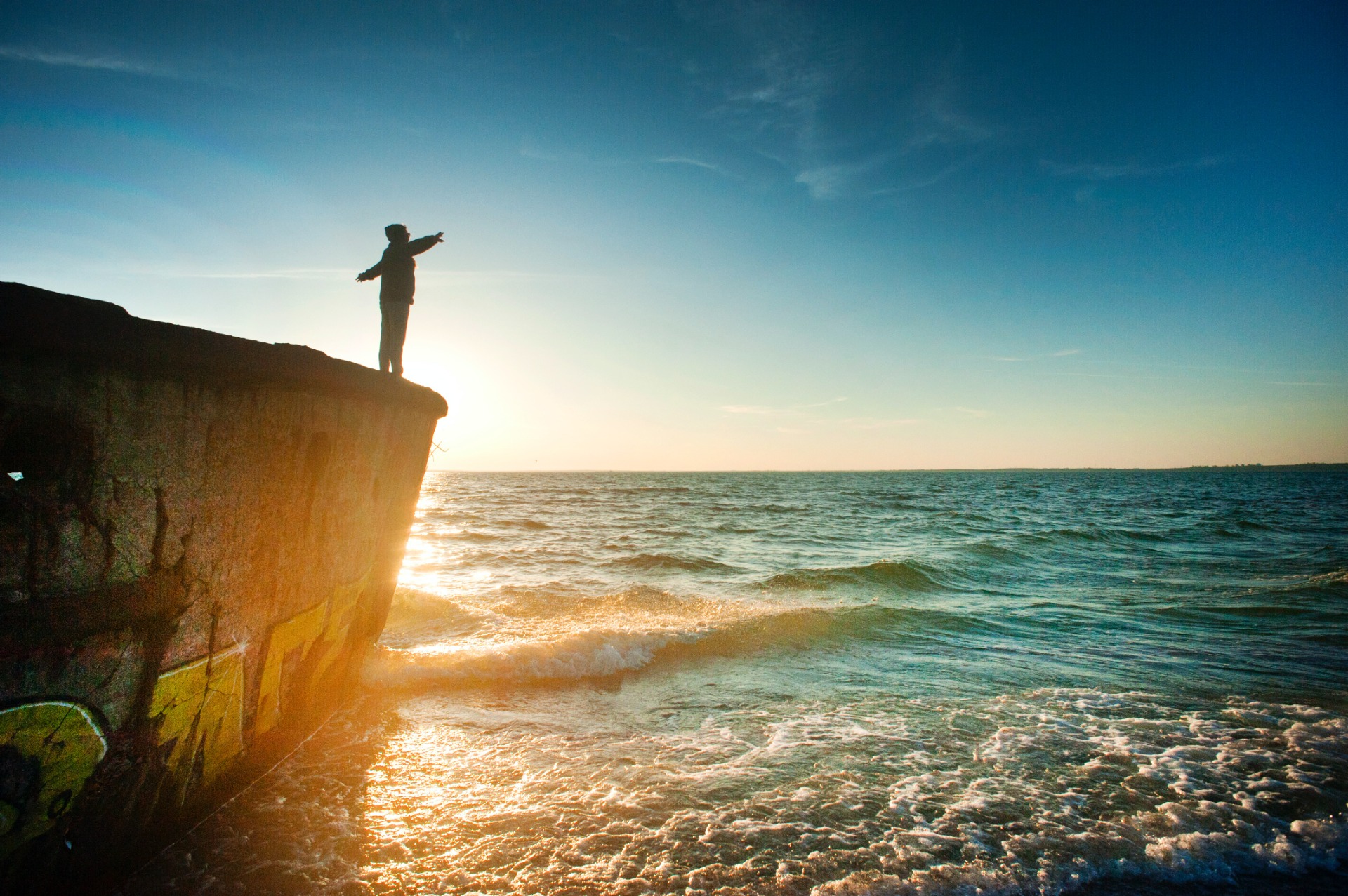 Una persona che guarda il mare al tramonto, tenendo le braccia aperte, libera dallo stress.